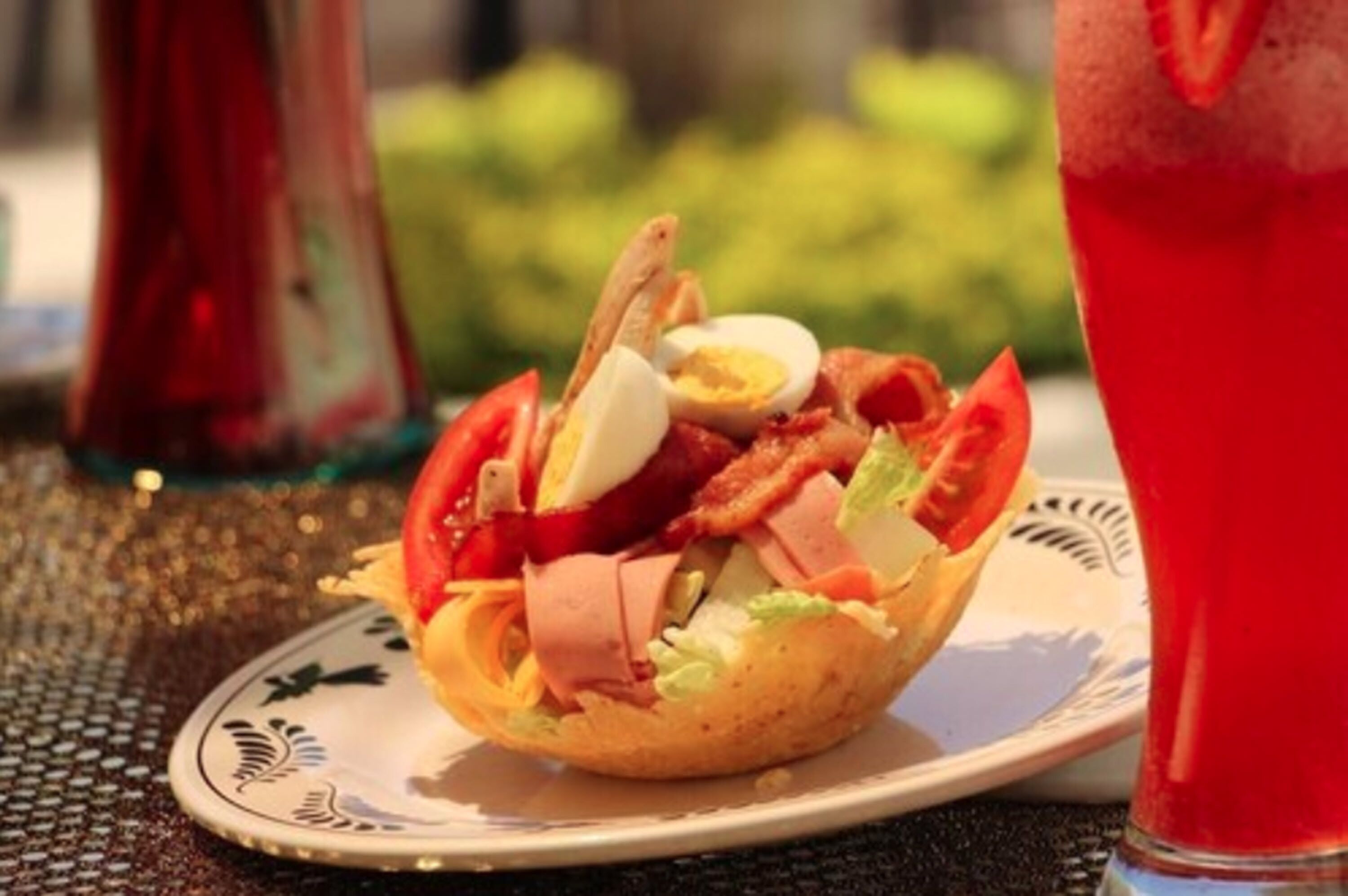 A salad in a bread bowl on a plate with a drink in the background.