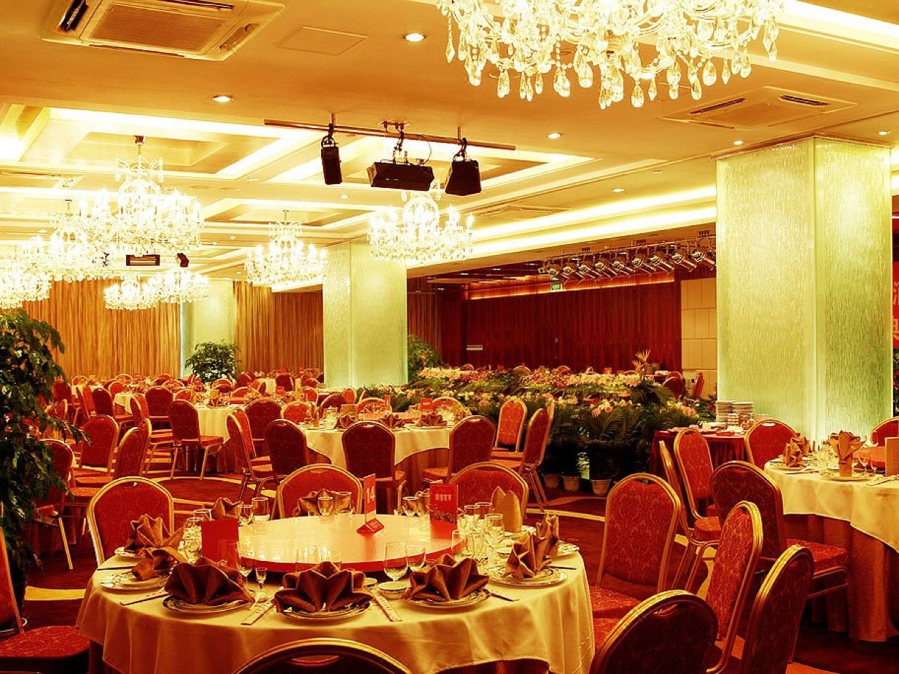 Un salón de banquetes con mesas redondas, sillas rojas, candelabros y una zona de escenario.