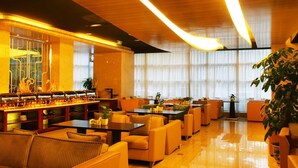 Et hotel lobby med en central buffet, siddeområder og store vinduer med gardiner.