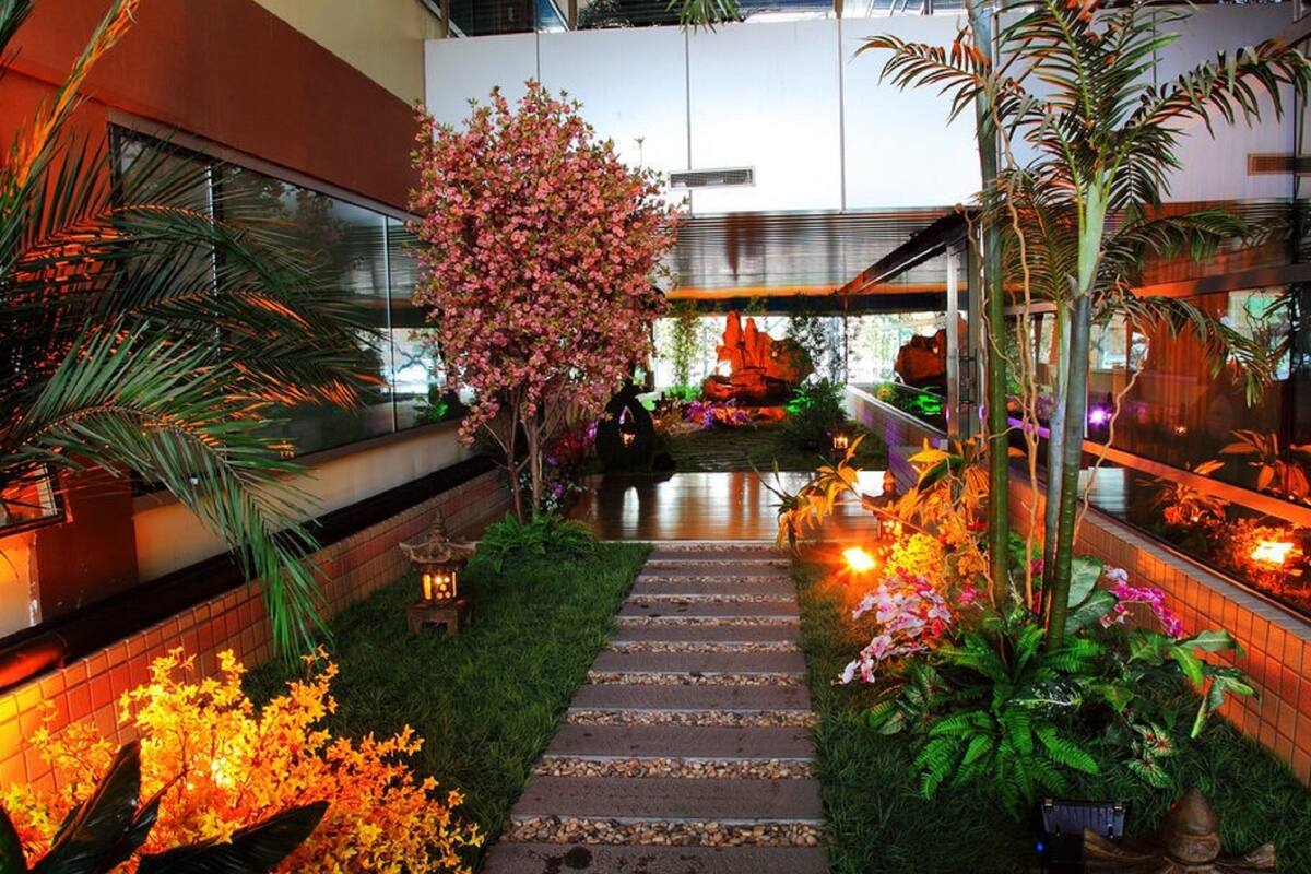 A well-lit indoor garden with a stone pathway, various plants, and a decorative lantern.