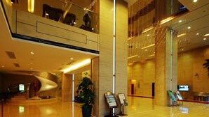 En moderne hotellobby med en buet reception, en stor stueplante og en digital informationsskærm.