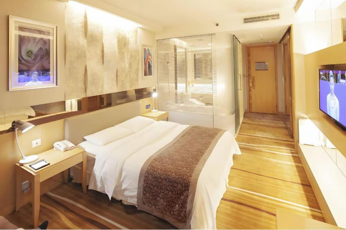 A hotel room with a bed, bedside table, lamp, and a television.