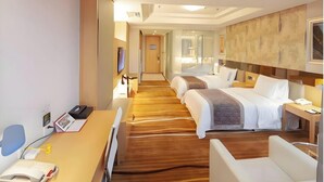Et hotelværelse med trægulv, to senge, et skrivebord med telefon og et fjernsyn på væggen.