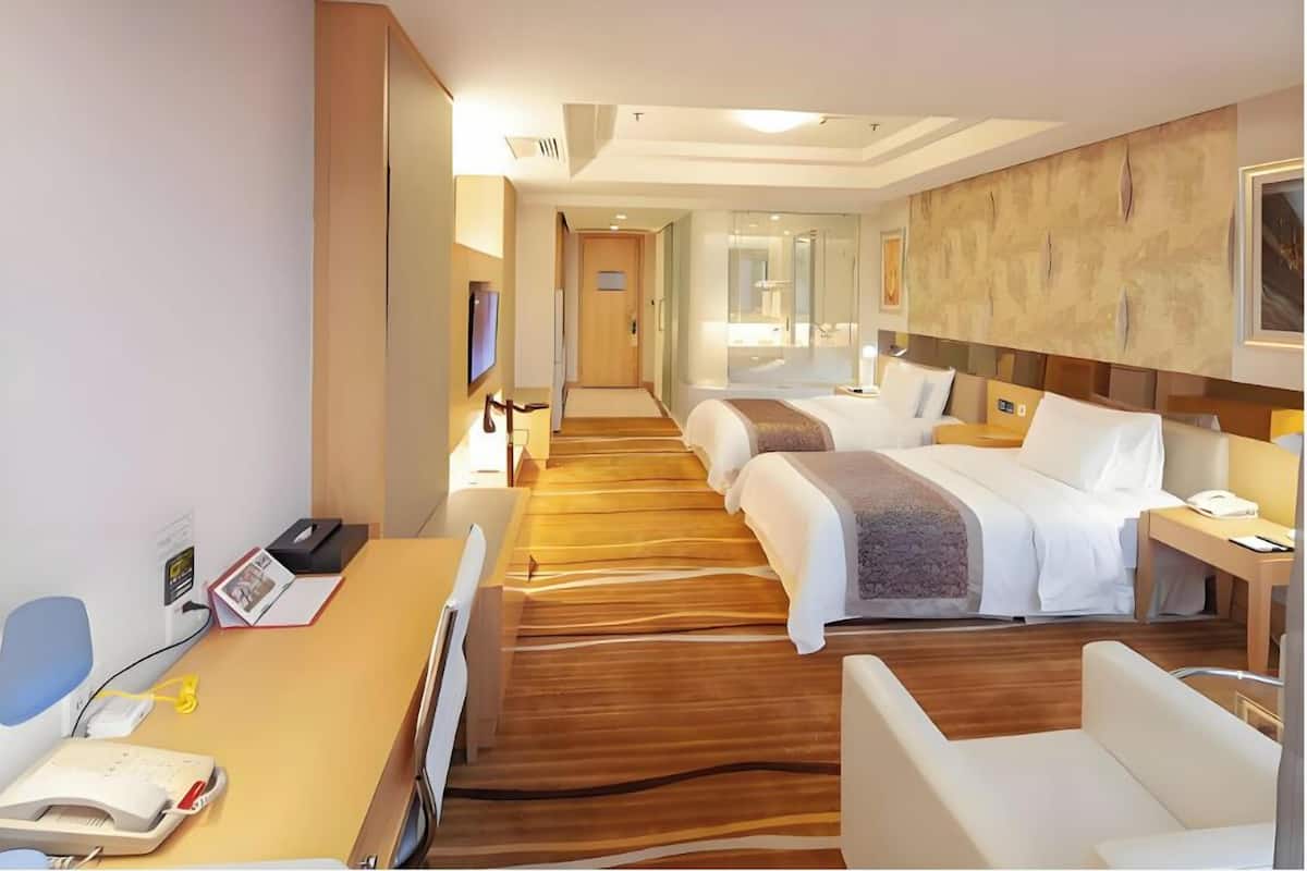 A hotel room with a wooden floor, two beds, a desk with a telephone, and a TV on the wall.
