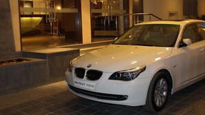 A white BMW car parked in front of a building with large windows and a modern interior. - Kapila Business Hotel (Pune)