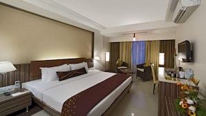 A hotel room with a large bed, a desk, a chair, a TV, and an air conditioning unit. - Kapila Business Hotel (Pune)