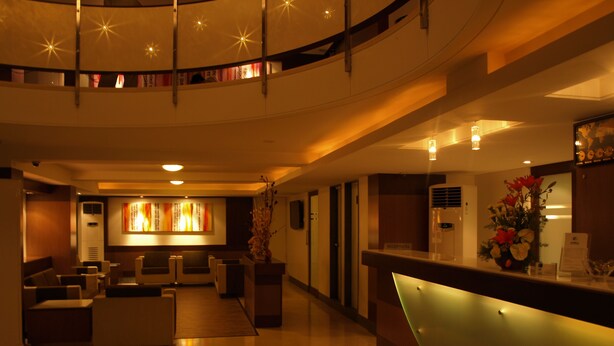 A hotel lobby with a reception desk, seating area, and a large wall with a decorative piece. - Kapila Business Hotel (Pune)