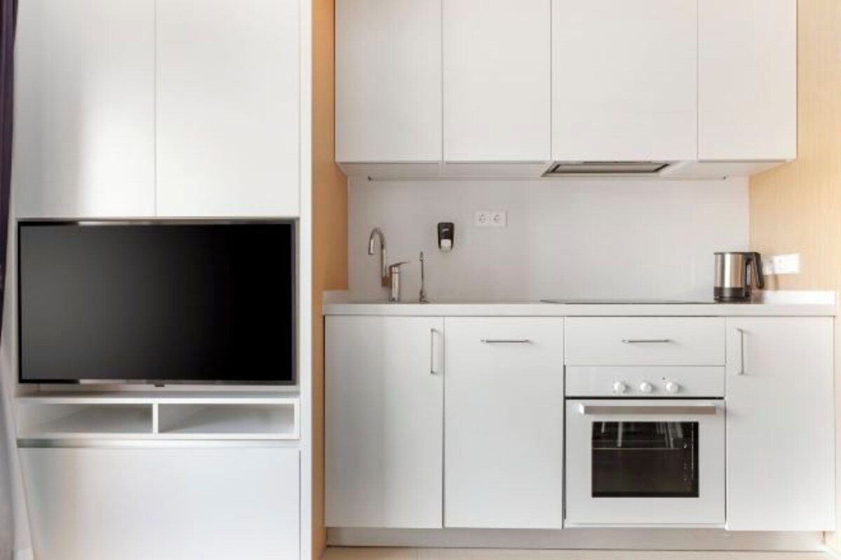 Uma cozinha moderna com armários brancos, forno embutido e televisão de tela plana.