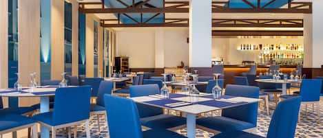 Un restaurant moderne avec des chaises et des tables bleues, un sol à motifs et un bar situé au fond de la salle.