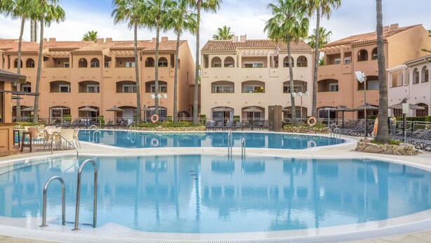 Una piscina rodeada de palmeras y un edificio con varios balcones.
