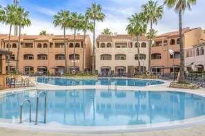 A swimming pool surrounded by palm trees and a building with multiple balconies. - Los Amigos Beach Club (Mijas)