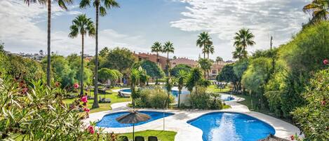 A resort with multiple swimming pools, palm trees, and a well-maintained lawn.
