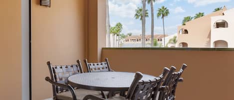 A round table with six chairs, a window with a view of palm trees and buildings, and a wall-mounted light fixture.
