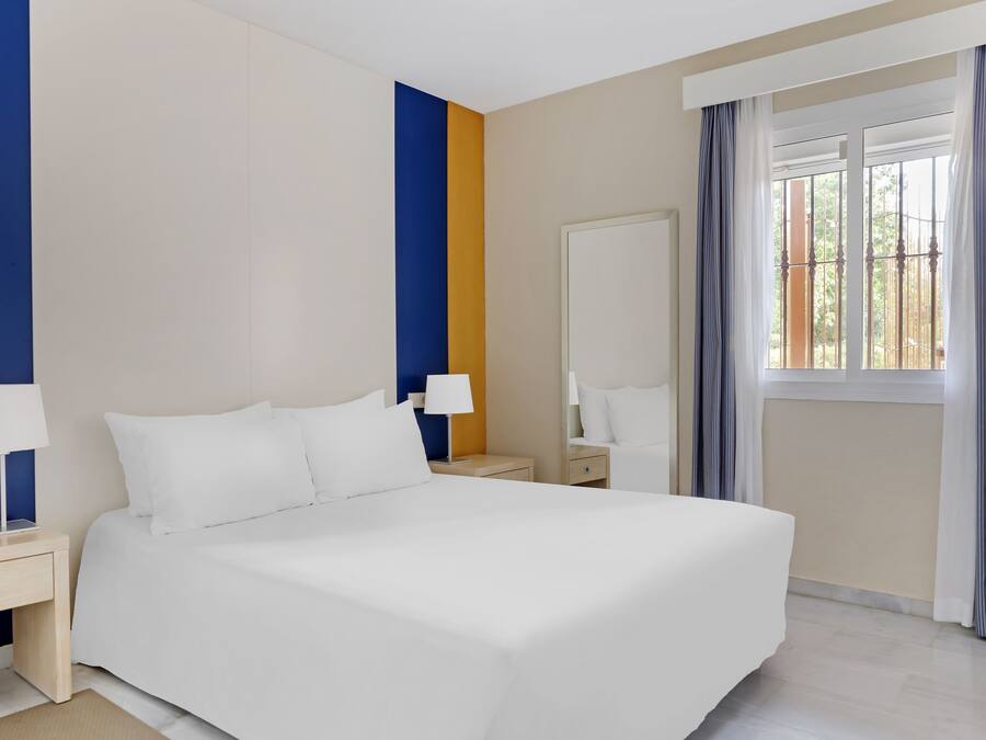 A hotel room with a large bed, two bedside tables with lamps, a wardrobe, and a window with curtains.