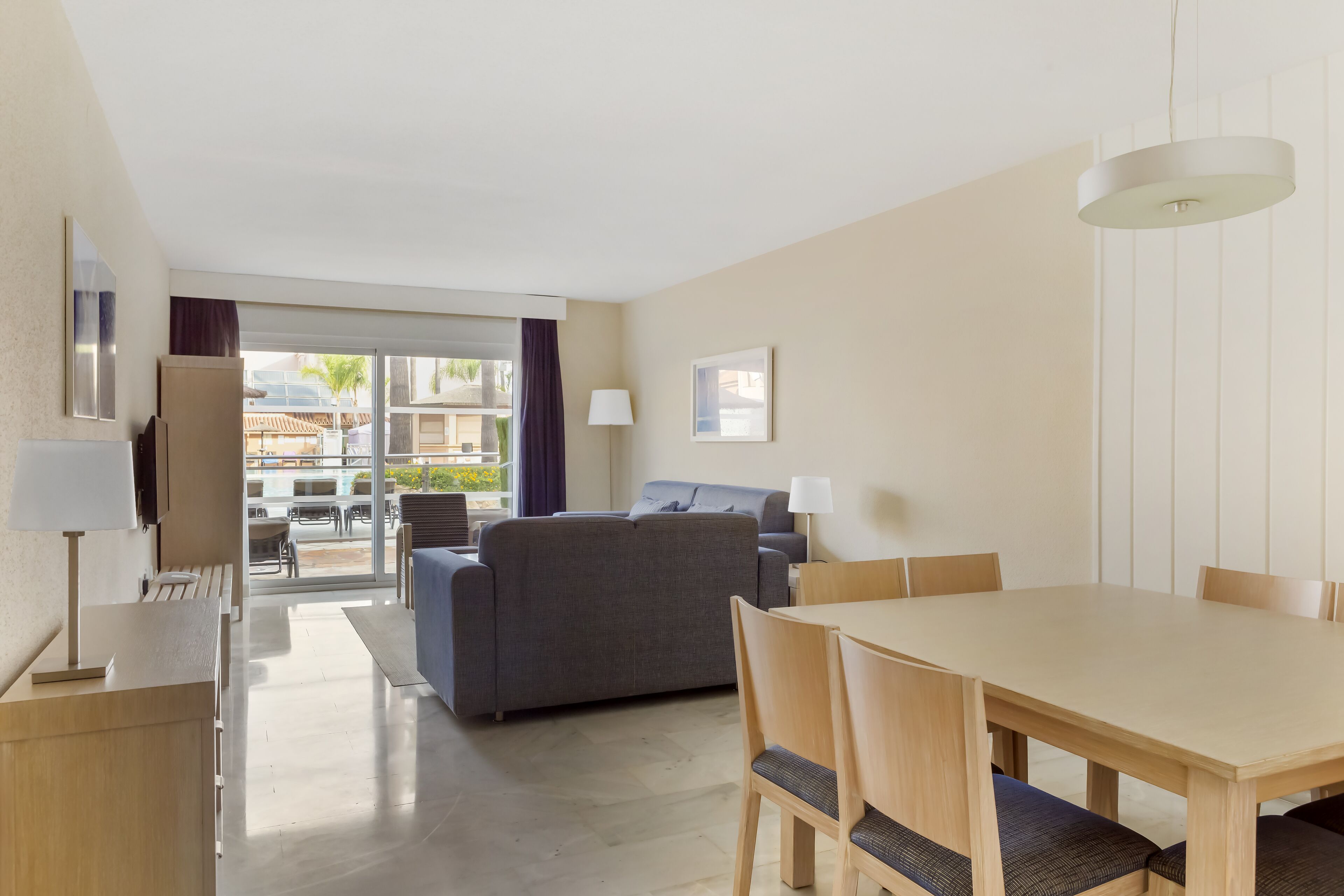 A modern hotel room with a dining area, a sofa, and a view of the outdoor patio.