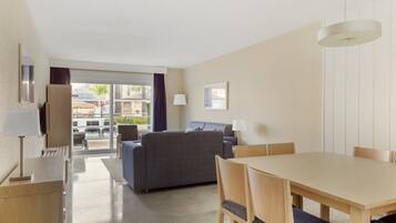 A modern hotel room with a dining area, a sofa, and a view of the outdoor patio.