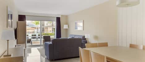 A modern hotel room with a dining area, a sofa, and a view of the outdoor patio.