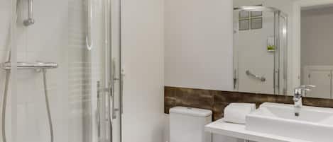 A modern bathroom with a glass-enclosed shower, a white toilet, and a large mirror above a white sink.
