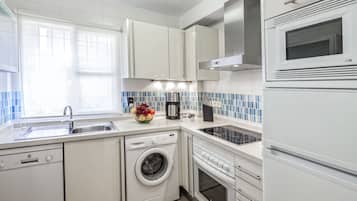 A modern kitchen with white cabinets, a built-in washing machine, a microwave, and a coffee maker.