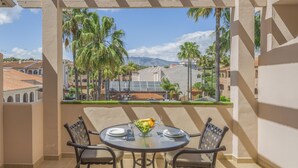 Un balcón con una mesa lista para dos personas, con vistas a un paisaje urbano con palmeras y edificios.