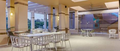 A spacious indoor area with tables and chairs, large windows, and a ceiling with skylights.