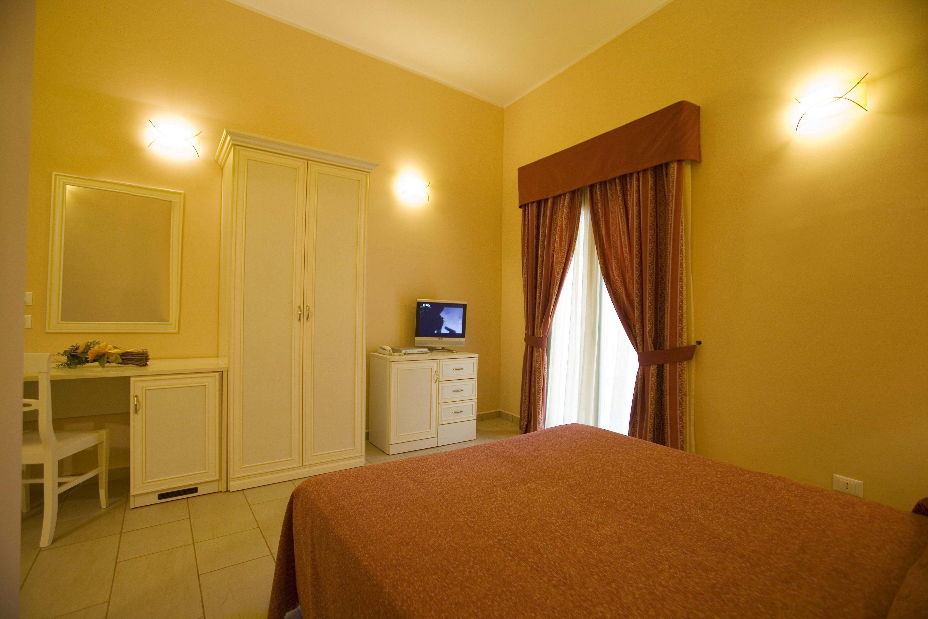 A bedroom with a bed, a desk, a television, and a wardrobe.