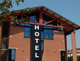 Un hotel con un llamativo letrero 'HOTEL', fachada de ladrillo, ventanas grandes y vigas estructurales rojas.
