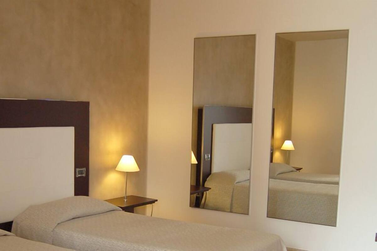 A hotel room with two beds, a nightstand with a lamp, and a large mirror on the wall.