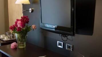 A hotel room with a flat-screen TV mounted on the wall, a vase with flowers on the table, a lamp, and a chair.