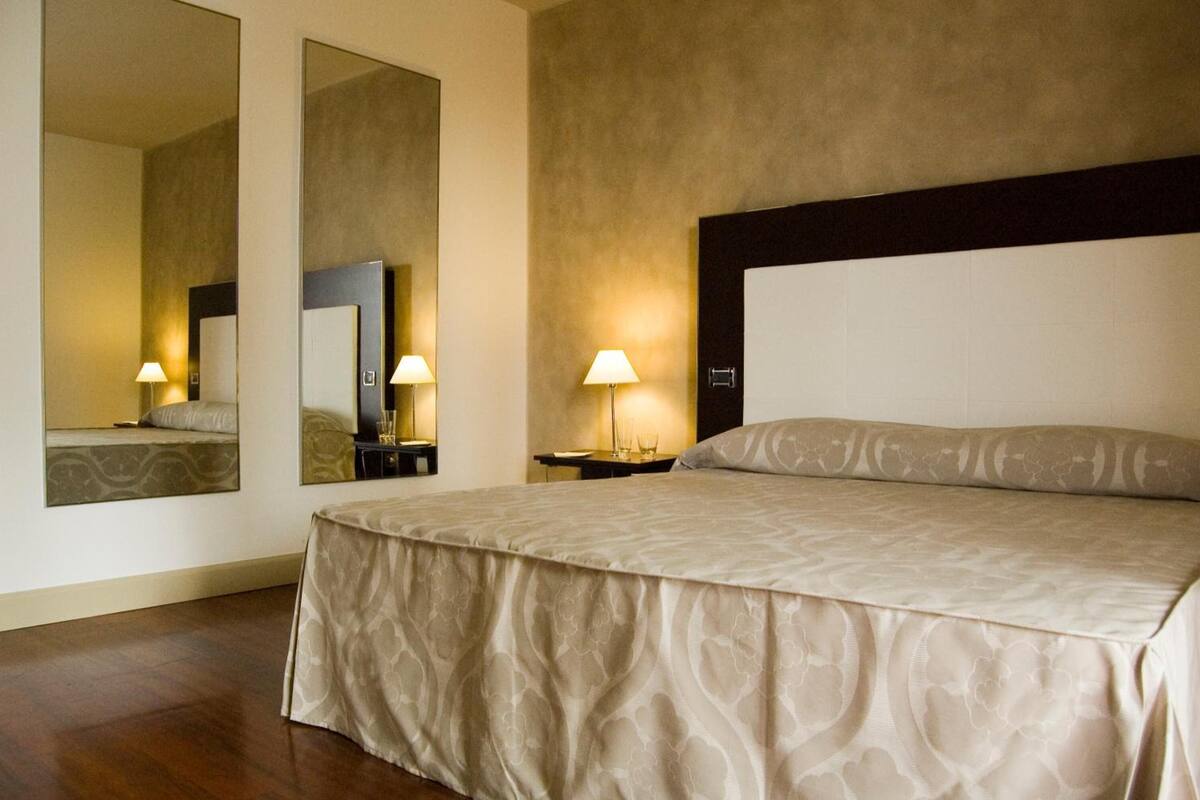 A hotel room with a large bed, two bedside tables with lamps, a large mirror, and a headboard.