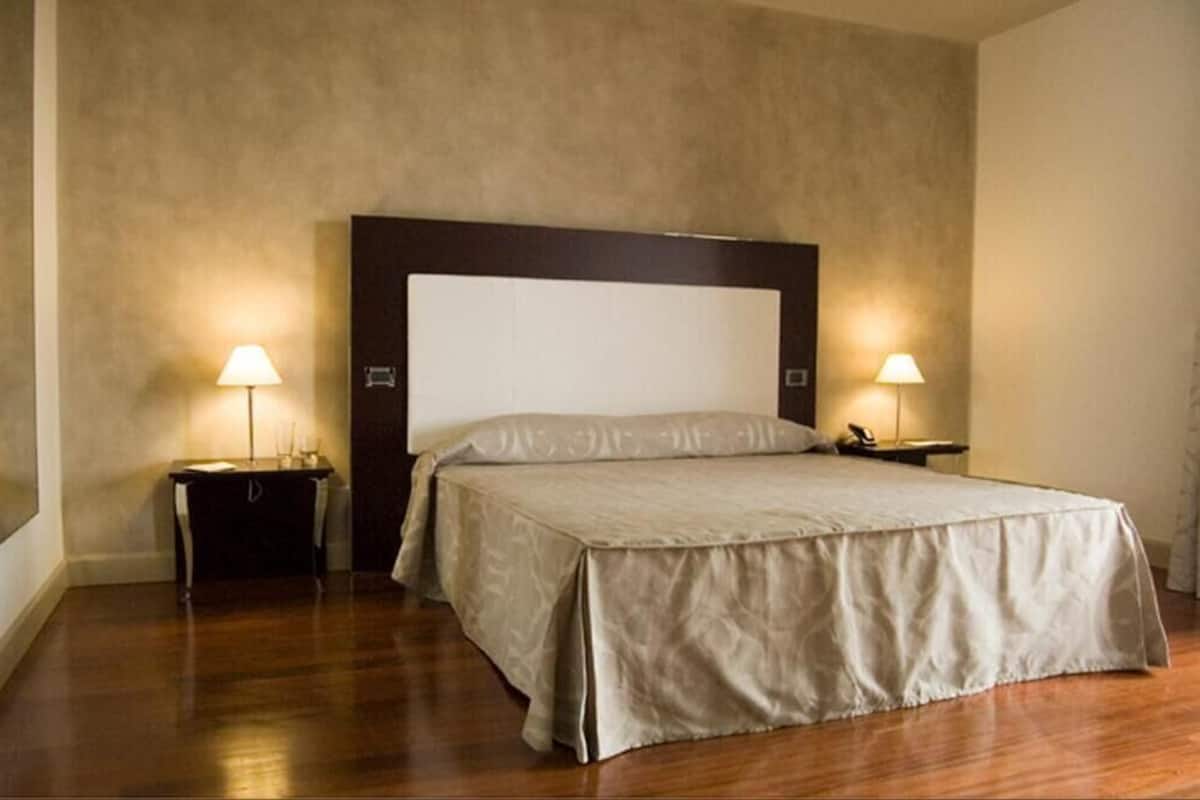 A hotel room with a large bed, two bedside tables with lamps, and a dark headboard.