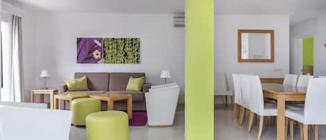A modern living room with a sofa, ottoman, dining table, and chairs.