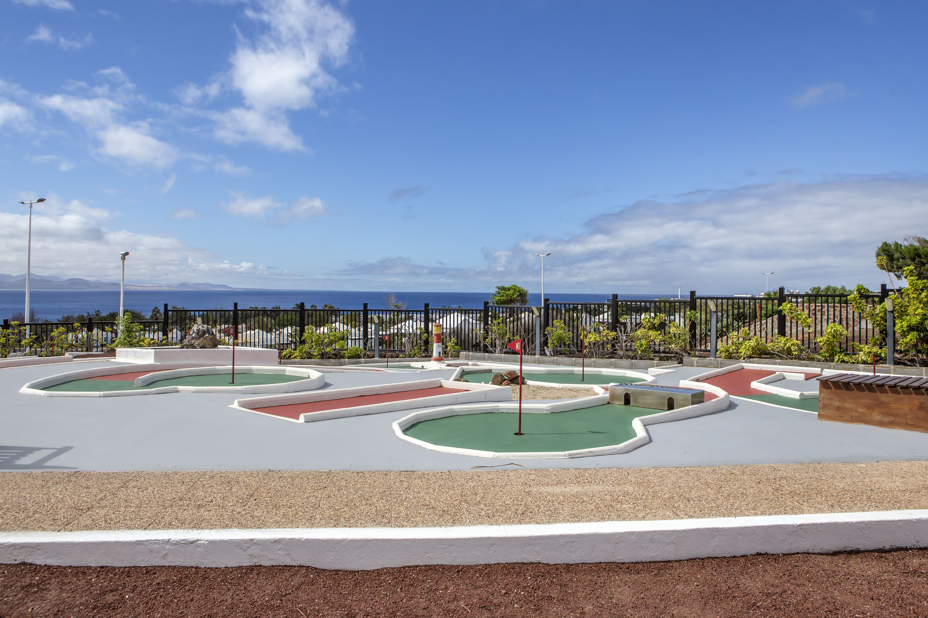 A miniature golf course with multiple holes, surrounded by a fence and greenery.