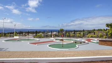 A miniature golf course with multiple holes, surrounded by a fence and greenery.