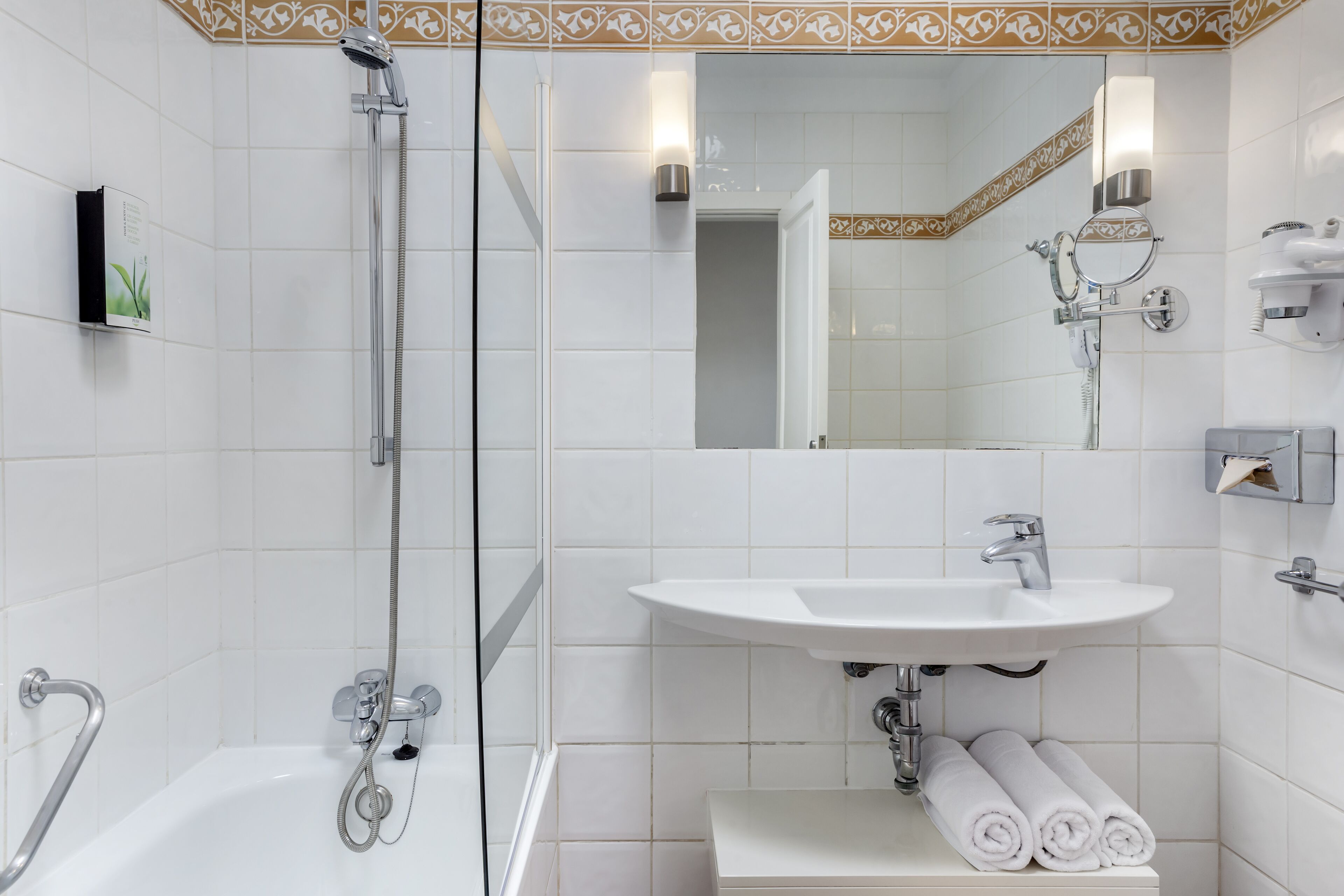 A modern bathroom with a glass shower enclosure, a white sink, and a mirror with a decorative tile border.