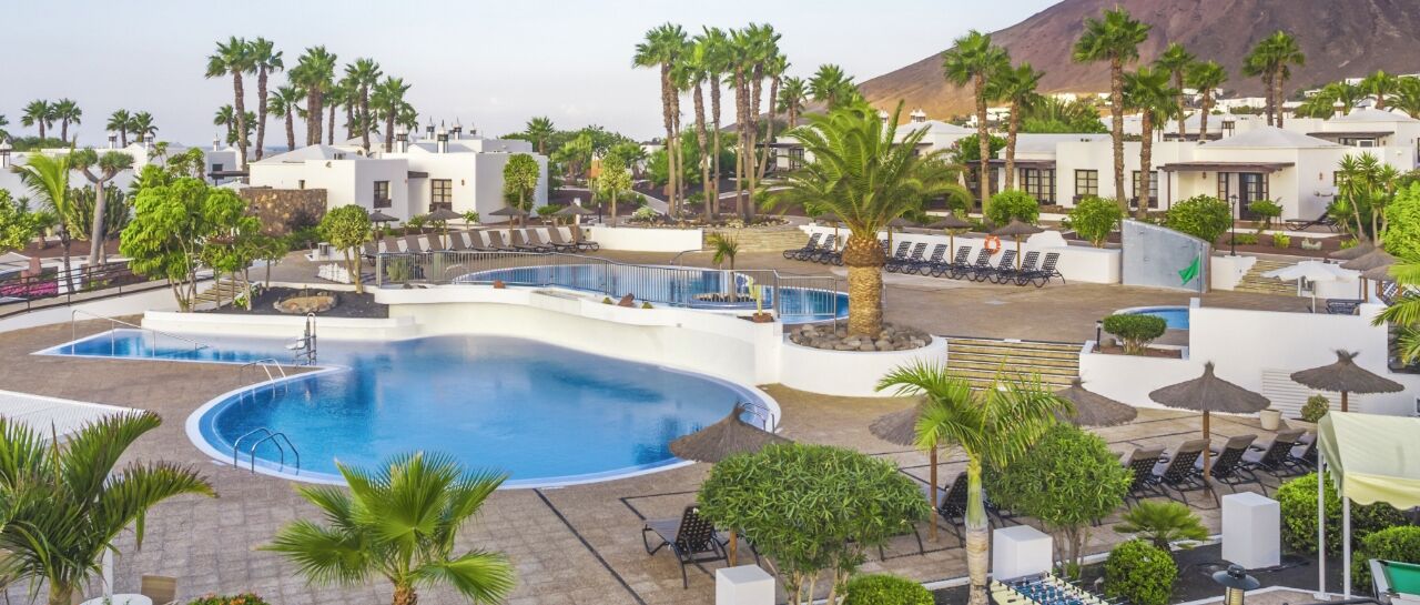 A resort with a large pool, palm trees, and white buildings.