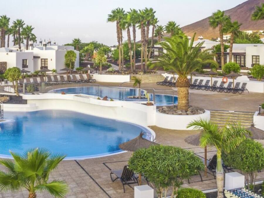 A resort with a large pool, palm trees, and white buildings.