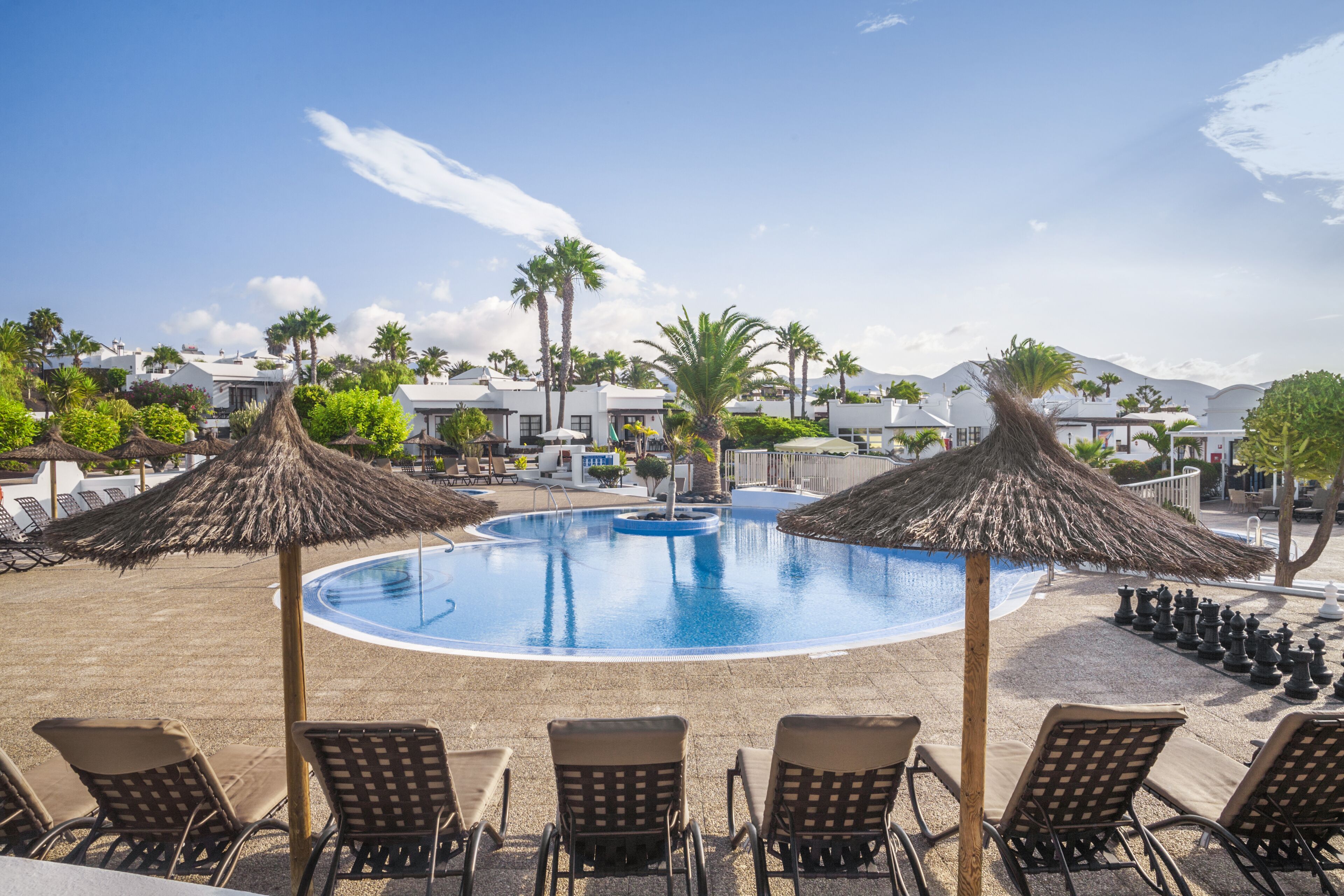 A pool area with lounge chairs and umbrellas, surrounded by palm trees and buildings.