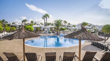 A pool area with lounge chairs and umbrellas, surrounded by palm trees and buildings.