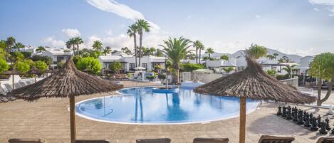 A pool area with lounge chairs and umbrellas, surrounded by palm trees and buildings.