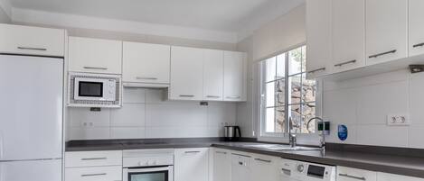 Une cuisine moderne avec des meubles blancs, un four encastré, un four à micro-ondes, un lave-vaisselle et un lave-linge.