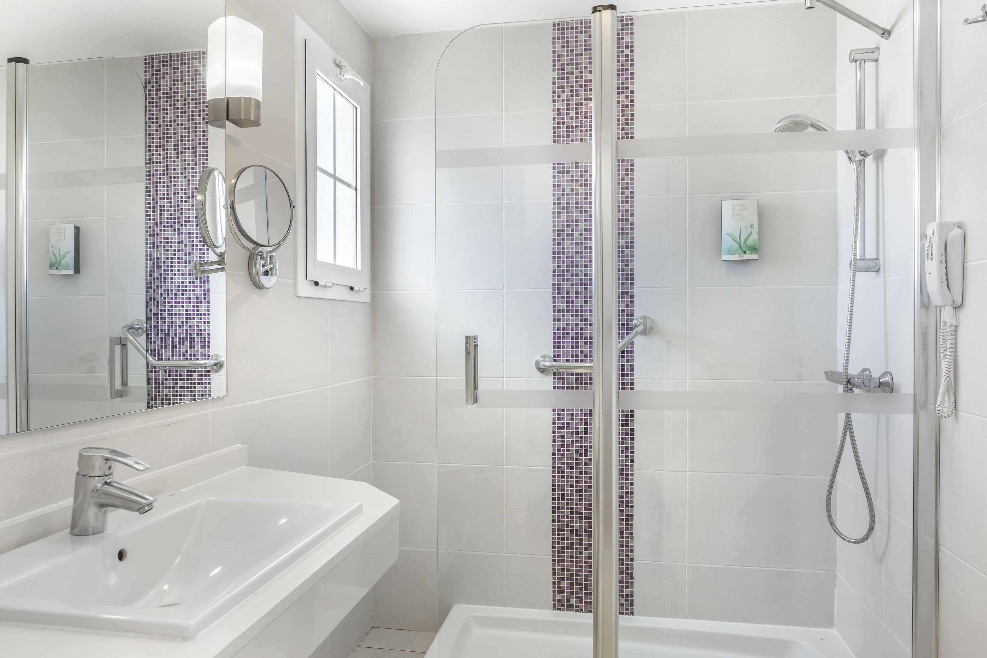 Een moderne badkamer met een wit wastafel, een douche met glazen wand en een betegelde muur met een paarse mozaïekstrook.