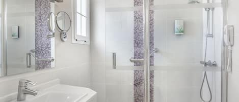 A modern bathroom with a white sink, a glass-enclosed shower, and a tiled wall with a purple mosaic strip.