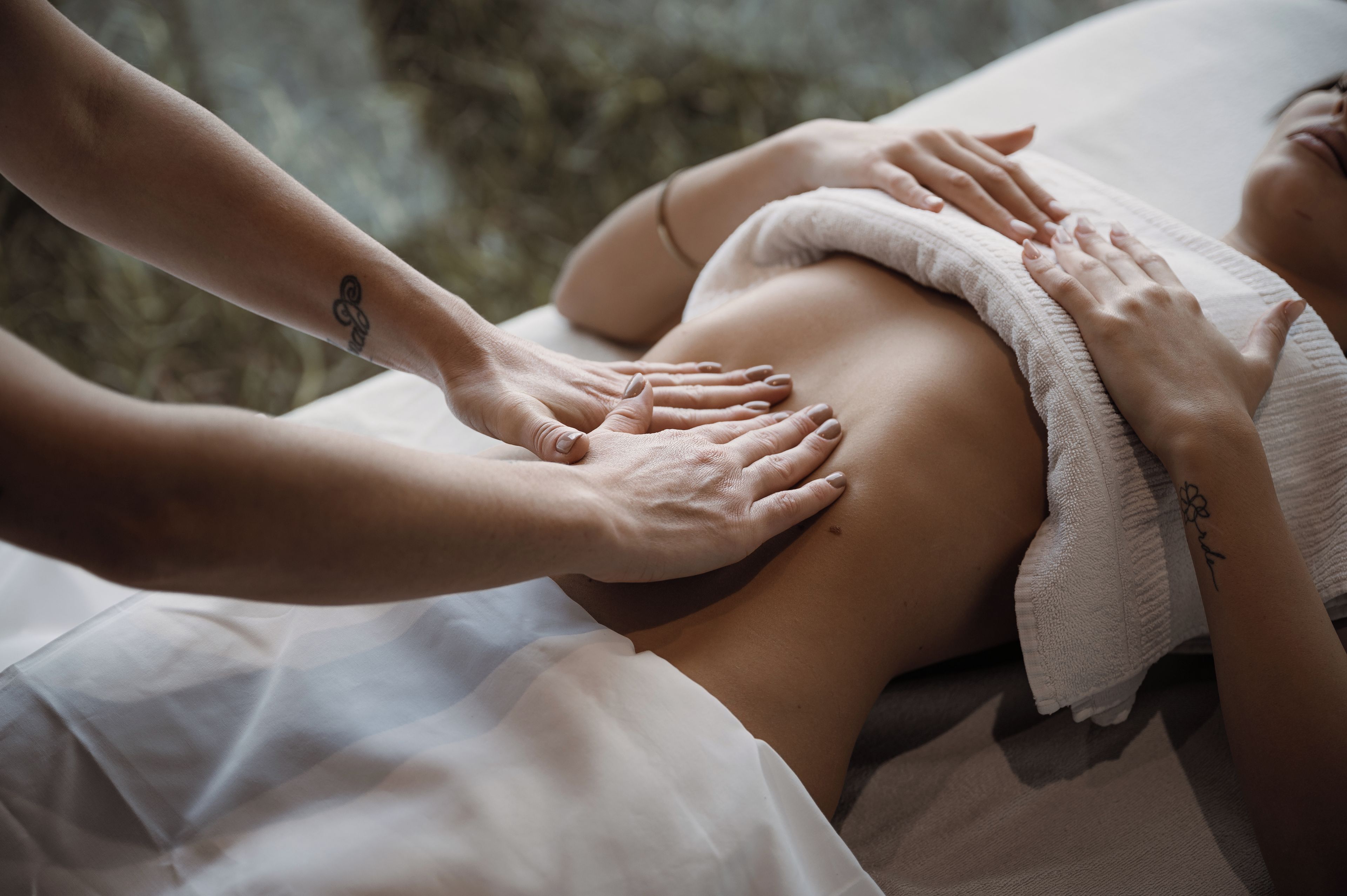 A person receiving a massage with hands on their back, a towel, and a tattoo on the masseuse's arm.