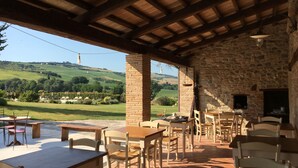 A rustic outdoor dining area with stone walls and wooden furniture, overlooking a scenic valley.