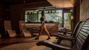 A modern interior with lounge chairs, a stone wall, and a view of greenery outside.