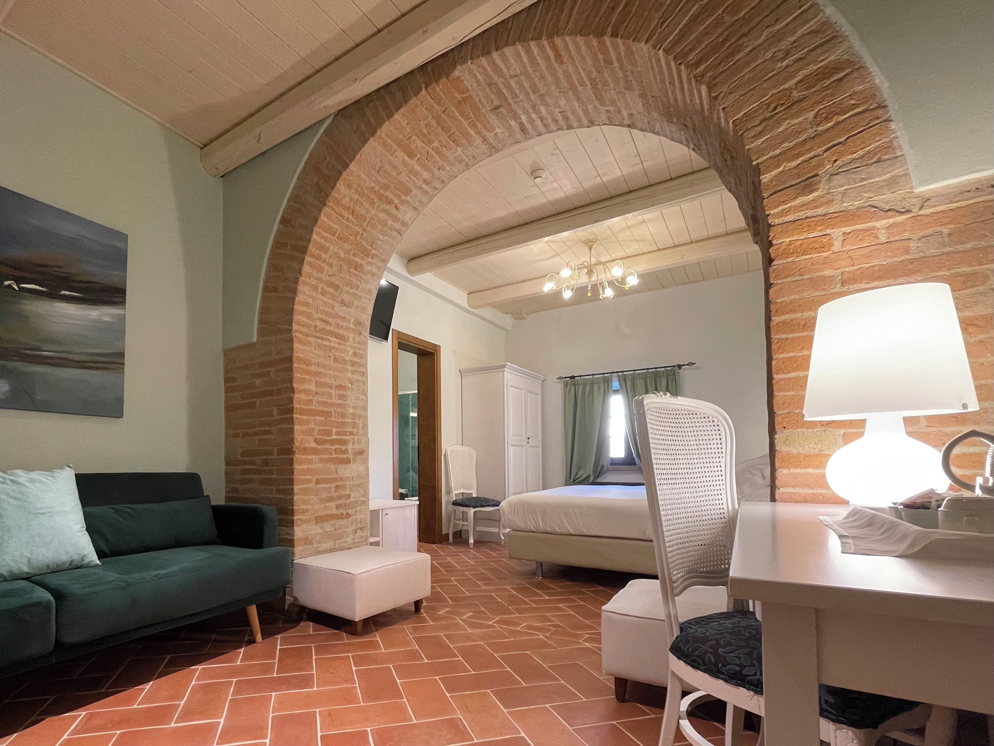 A room with a brick archway, a bed, a chair, a table, and a painting on the wall.