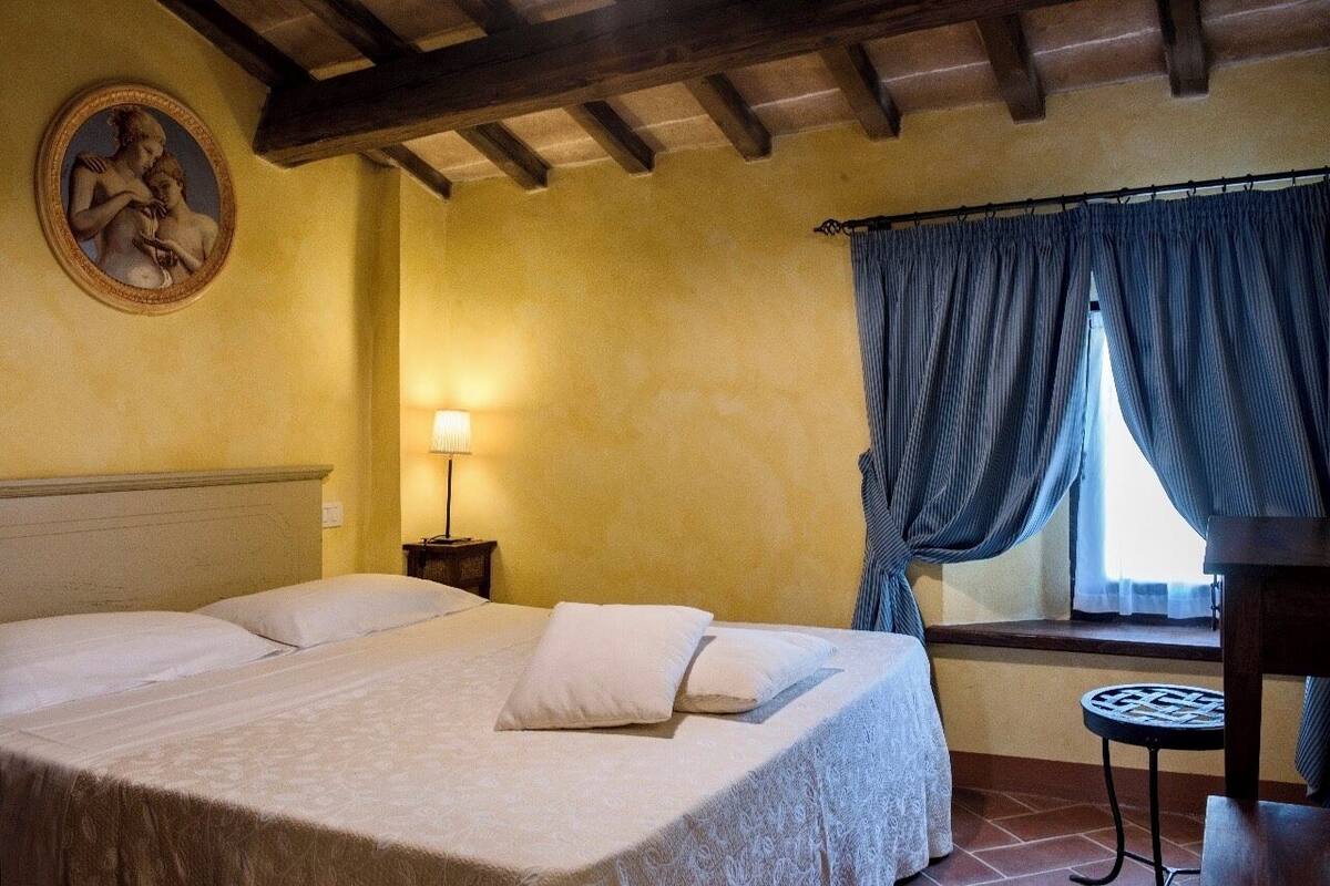 Un dormitorio con cama, mesita de noche, lámpara y ventana con cortinas.