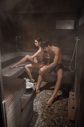 A sauna with two people sitting on benches, steam visible, and a tiled floor. - Ca' Virginia - Guest House (Montecalvo in Foglia)