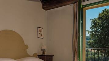 Ein Schlafzimmer mit einem großen Bett, einem Nachttisch, einer Lampe, einem gerahmten Bild und Blick auf Grün durch ein Fenster.